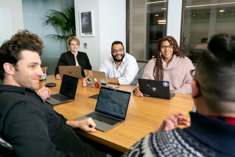 Colleagues sitting around a conference table with laptops smiling