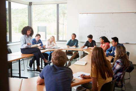 Teacher sitting on a desk talking to a group of students