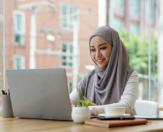 Woman wearing a hijab sitting at her computer in a quiet coffee shop
