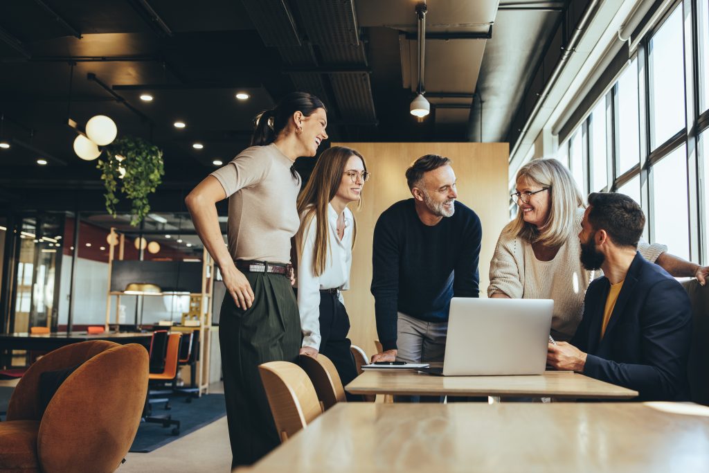 Smiling businesspeople having a discussion while collaborating on a new project in an office. Group of happy businesspeople using a laptop while working together in a modern workspace.