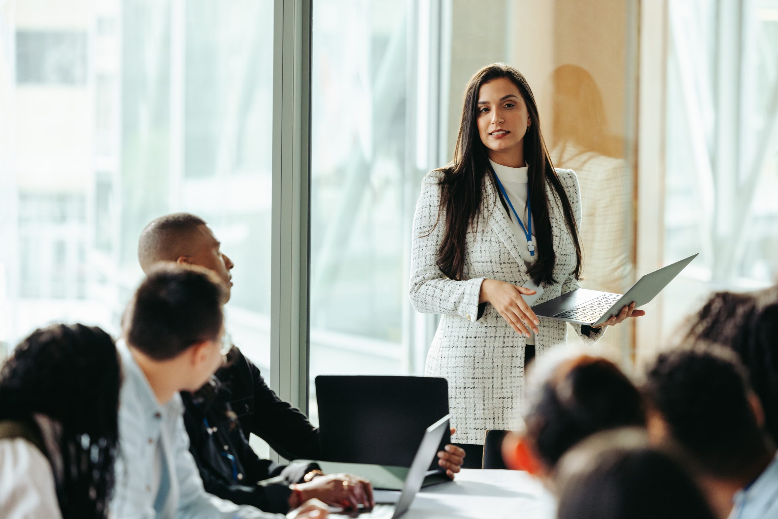 Female business leader confidently presents during a board meeting, showcasing strategies to a diverse team in a modern office environment.